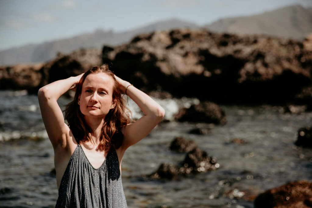 Frau hat die Hände am Kopf, sitzt vor dem Meer vor Felsen auf Teneriffa