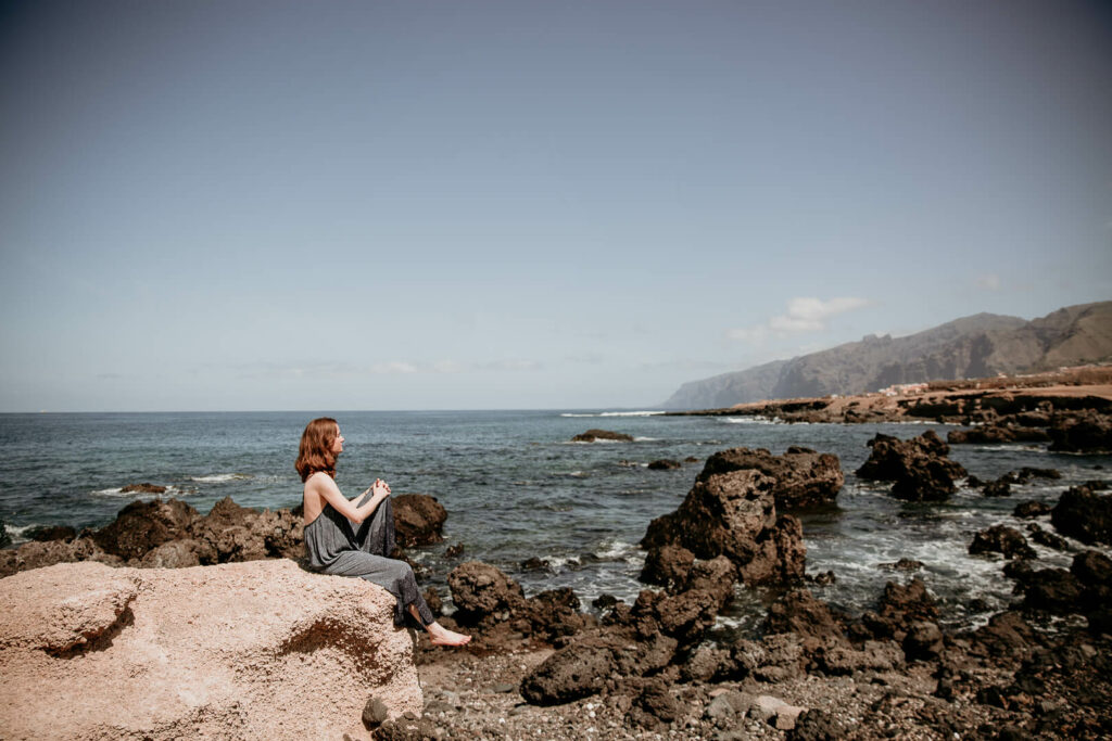 Eine Frau sitzt auf einem Felsen am Meer mit Steinküste und schaut in die Ferne